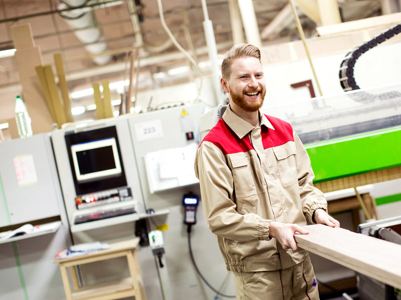 Smiling factory worker moving word to machine to produce skis