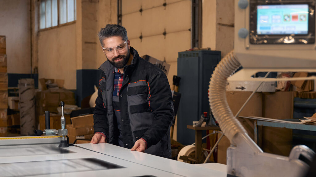 DPS Skis Case Study Featured Image - Smiling man plains wood using factory machine to produce skis