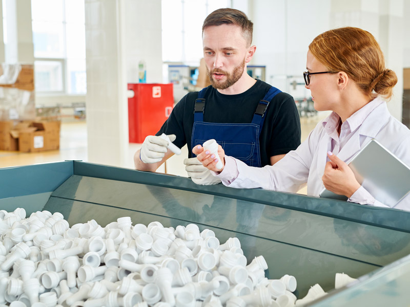 Two workers reviewing plastic components and discussing different types of BOM in manufacturing