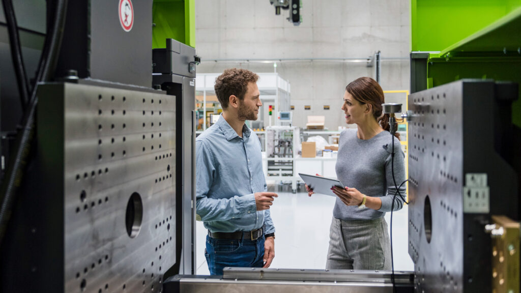 Holmgrens Plast Case Study Featured Image shows man and woman discussing manufacturing operations with internal view of factory machinery