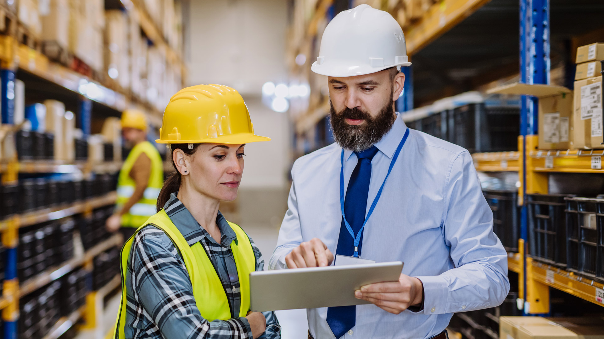 Male and female coworker discuss inventory and wms warehouse management system configuration between aisles in warehouse