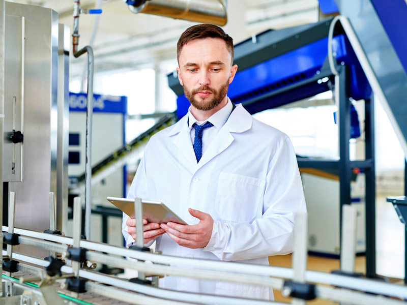 Worker in lab coat assess factory production line to revview the real-time integration of software in the medical device component factory