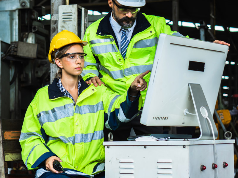 Two workers use computer in factory to manage entire manufacturing operation