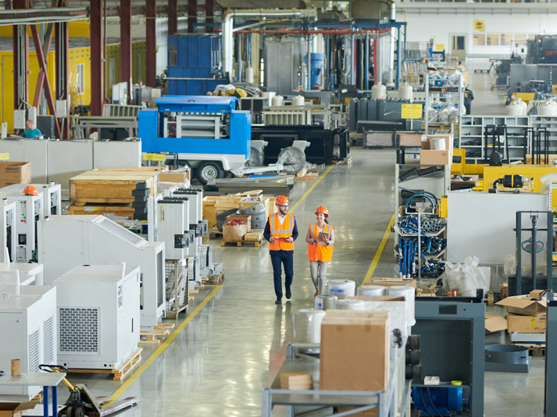 Male and female worker discuss driving operational improvements whilst walking along plastic factory shop floor