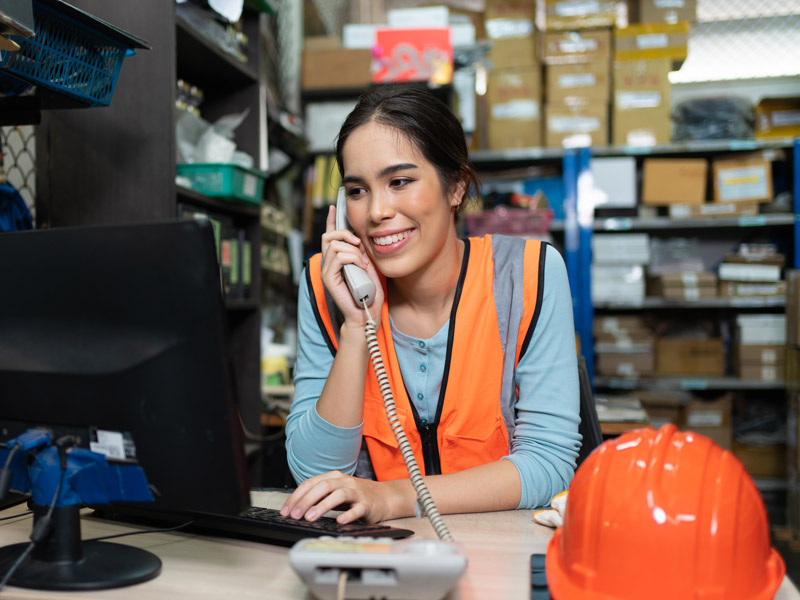 Female manufacturing worker in office wearing high vis jacket provides sales quotes to customers over the phone