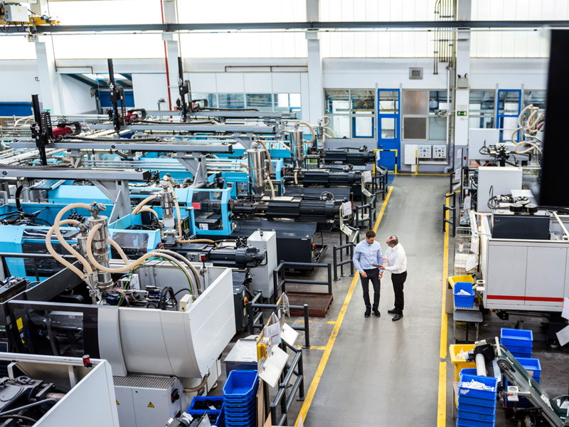 Two workers discussing on the factory shop floor as machines continue to produce goods round the clock