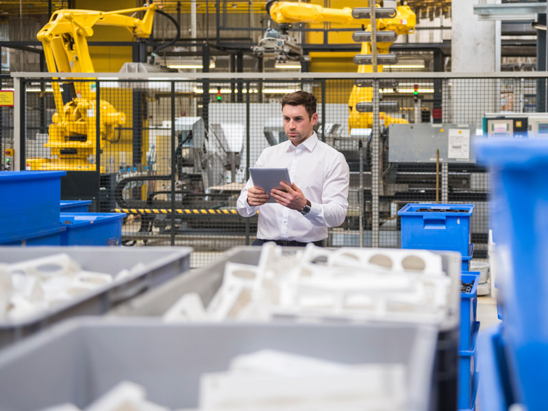 Worker in a suit stood next to plastic manufactured products consulting manufacturing ERP on a tablet