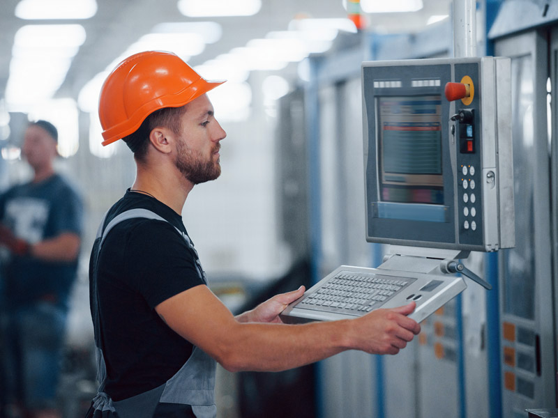 Factory worker operates computer on manufacturing machine, using ERP software