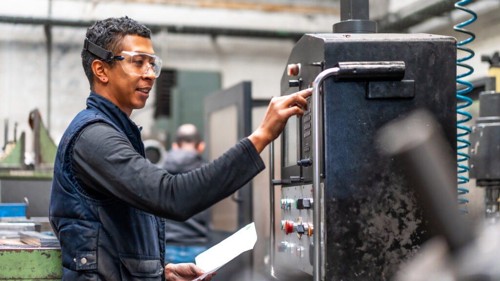 Factory worker smiling and operating machinery using standardisation of manufacturing processes