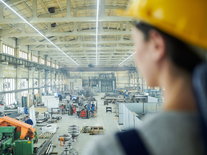 female factory worker looks out over the factory floor to oversee the standardisation of manufacturing processes